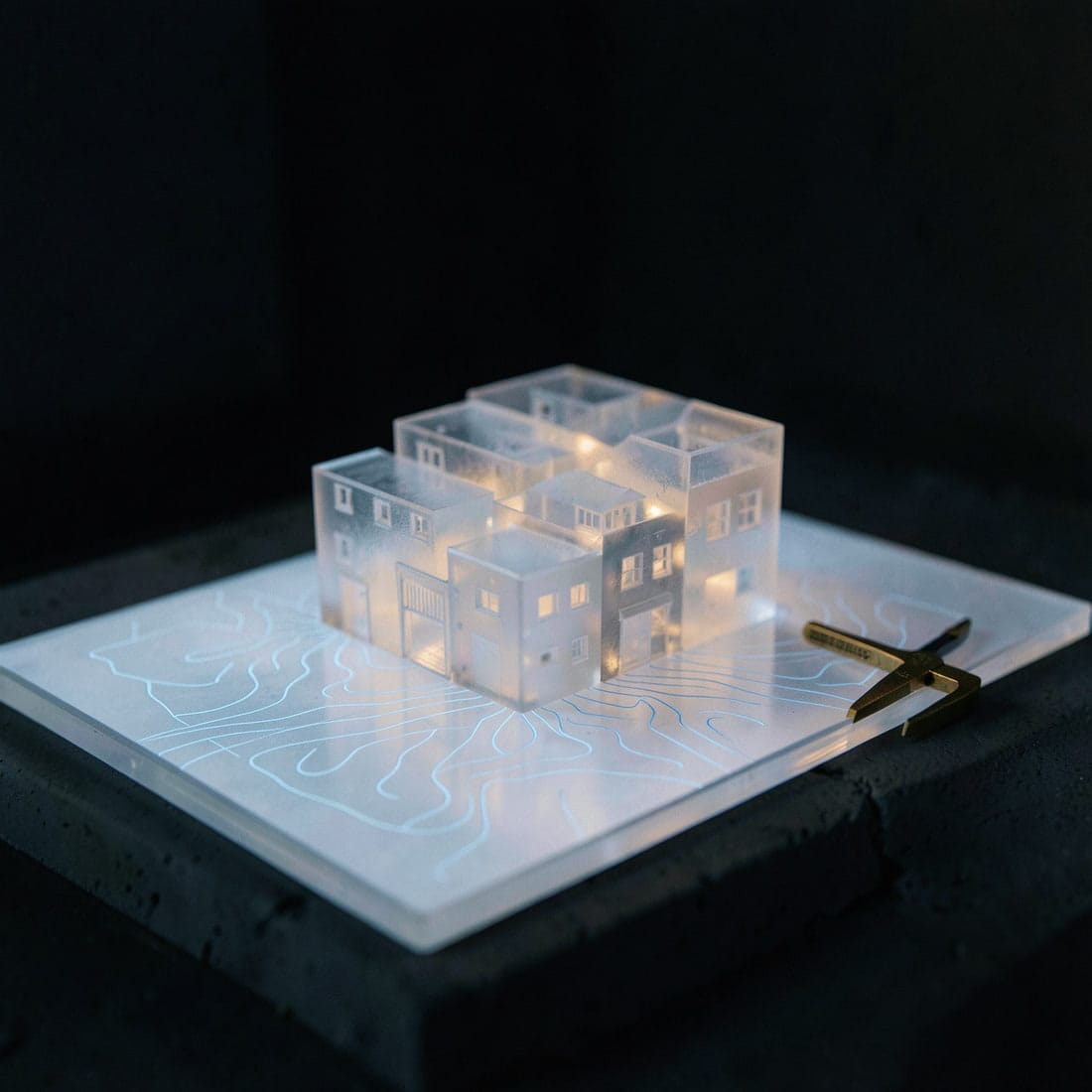 Translucent model of a neighbourhood on a light table, with survey contour lines projected across it.